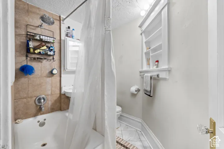 Built-in recessed shelving, wall-mounted vanity lighting, tiled flooring, bathtub with shower fixture, and tiled shower surround