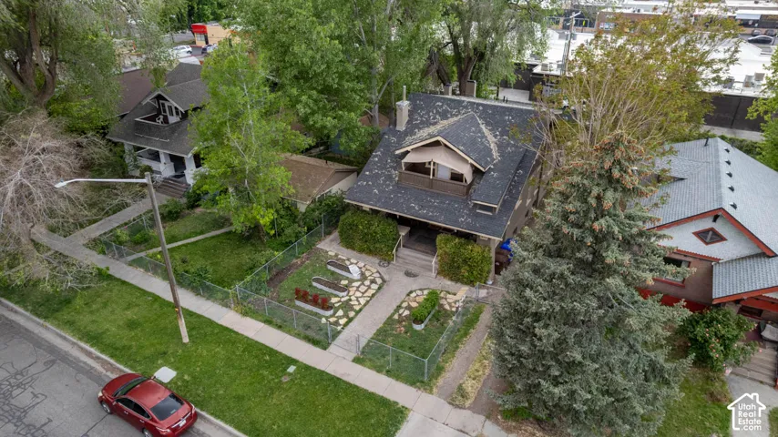 Gabled roofline with a dormer, mature trees, landscaped front yard with stepping stones, and a fenced perimeter