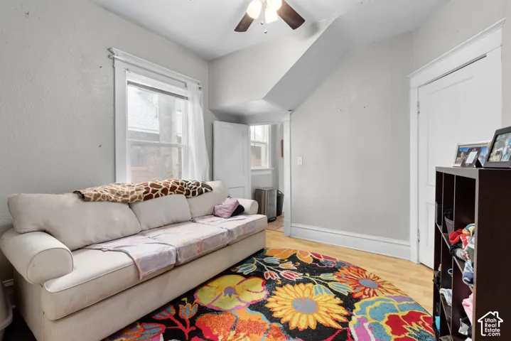 Wood-finish flooring with light-toned walls, featuring a window with white trim, and a ceiling fan with light fixture