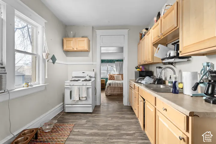 Kitchen featuring wood-finish flooring, light wood cabinetry, a double basin sink, and a white gas range