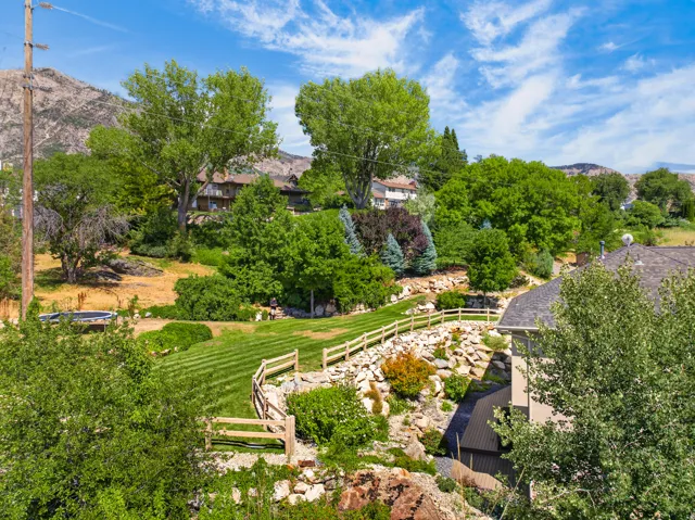 Expansive terraced yard featuring a manicured lawn, established landscaping, and a rustic wooden fence