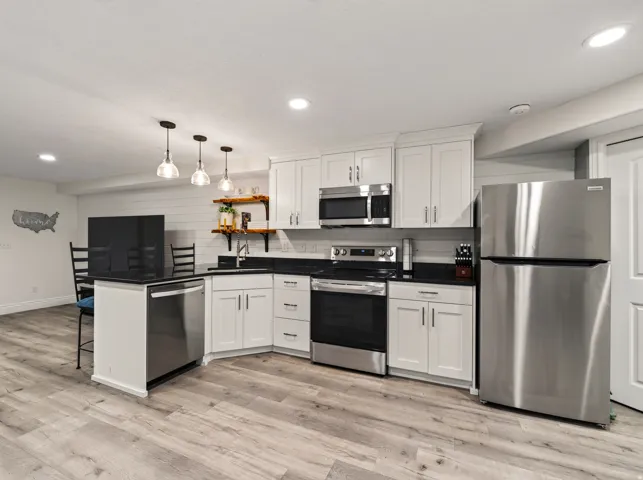 Kitchenette featuring stainless steel appliances, white cabinetry, dark countertops, and wood-finish flooring