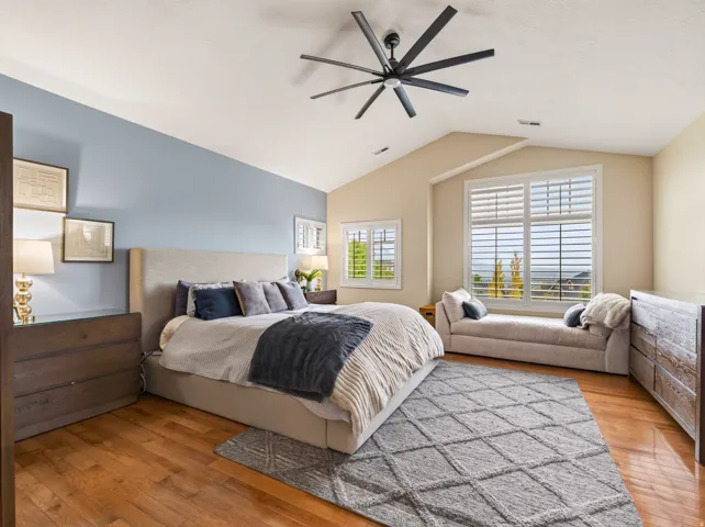 Vaulted ceiling with a contemporary ceiling fan, wood-finish flooring, and multiple windows with plantation shutters