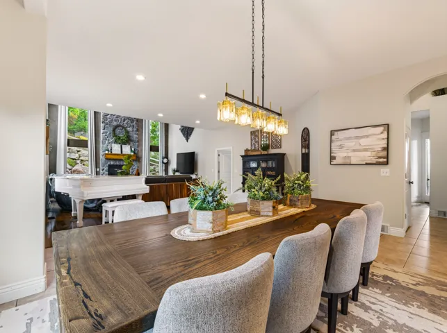 Wood-finish dining table with upholstered seating, linear chandelier with amber glass shades, vaulted ceiling, and recessed lighting
