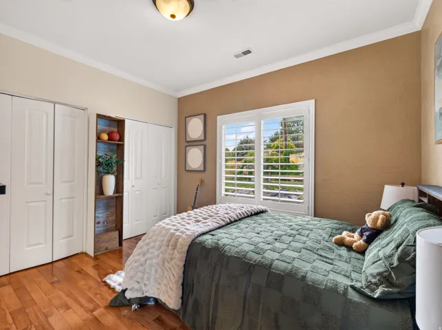 Hardwood-finish flooring, built-in shelving, white plantation shutters, white bi-fold closet doors, and crown molding