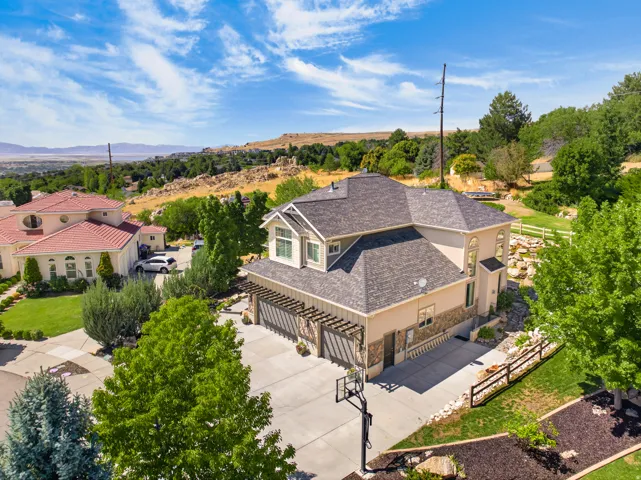 Multi-level residence featuring a dark shingle roof, stucco and stone-veneer exterior, and a two-car garage with a wood pergola