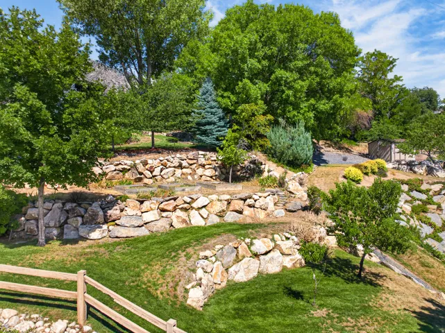 Tiered landscaping featuring natural stone retaining walls, mature trees, and a wooden fence