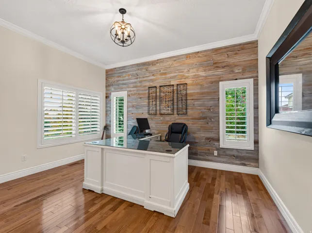 Hardwood flooring, crown molding, plantation shutters, reclaimed wood accent wall, and a built-in white desk with a dark countertop