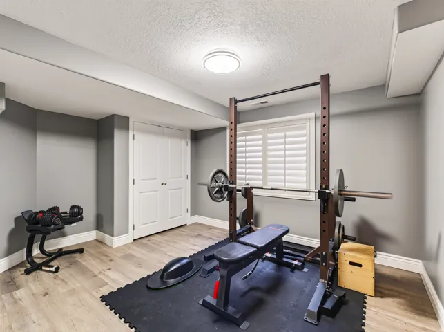 Recessed window with plantation shutters, light wood-finish flooring, neutral gray walls, bright ceiling light fixture, and white bi-fold doors