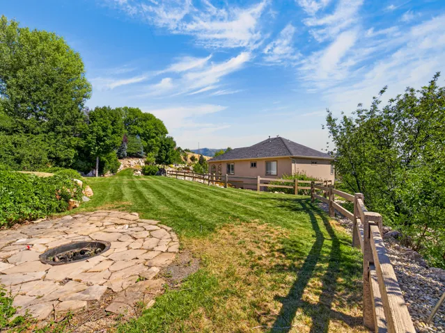 Expansive lawn area with a flagstone fire pit, surrounded by mature trees and a rustic wooden fence
