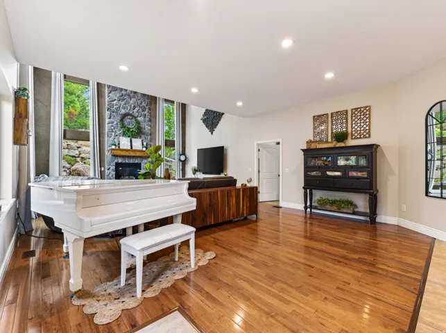 Hardwood flooring throughout, recessed lighting, stone fireplace with mantel, built-in media console, and large windows