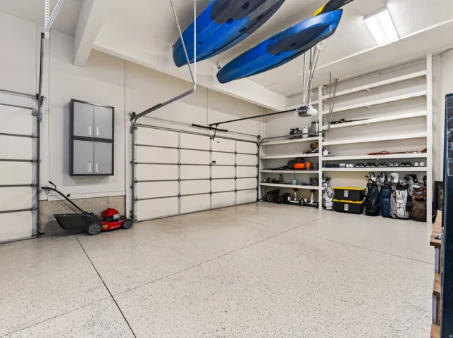 Garage featuring two overhead doors, built-in shelving, mounted cabinetry, and a finished floor