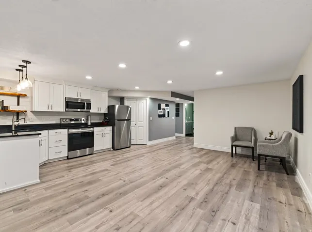 Kitchenette with white cabinetry, stainless steel appliances, dark countertops, and wood-finish flooring throughout