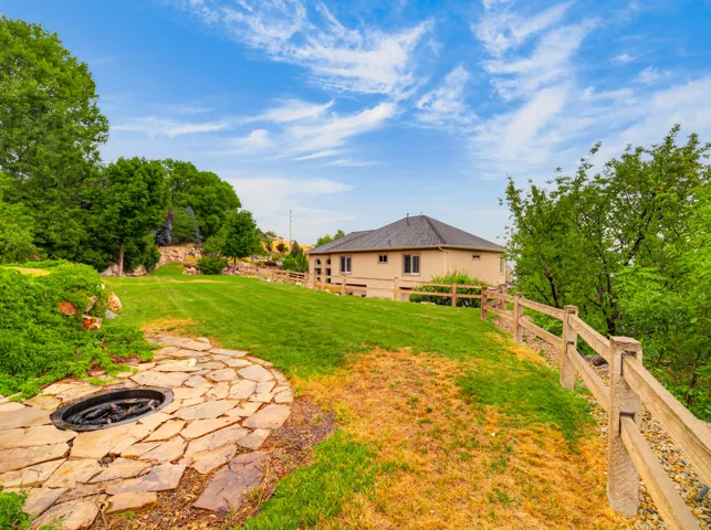 Expansive backyard featuring a manicured lawn, established trees, and a flagstone patio with a fire pit