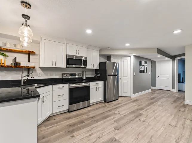 White cabinetry, stainless steel appliances, black countertops, wood-finish flooring, and recessed lighting ADU Kitchen