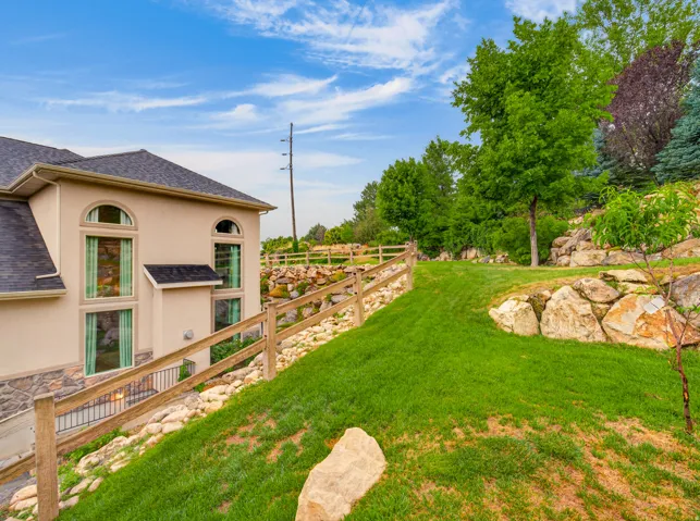Sloping lawn with a wooden fence, rock retaining walls, and mature trees