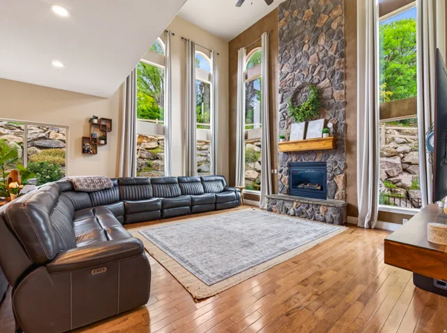 Spacious living area featuring high ceilings, wood-finish flooring, a stone-clad fireplace with mantel, and tall arched windows
