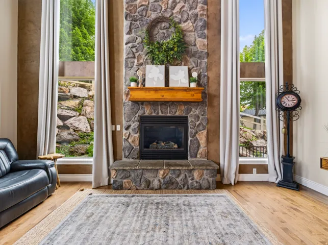 Stone-clad fireplace with a wood mantel, flanked by two full-height windows, and wood-finish flooring