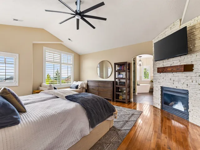 Hardwood flooring, vaulted ceiling, multi-pane windows with plantation shutters, stacked stone fireplace with wood mantel, and an arched entry