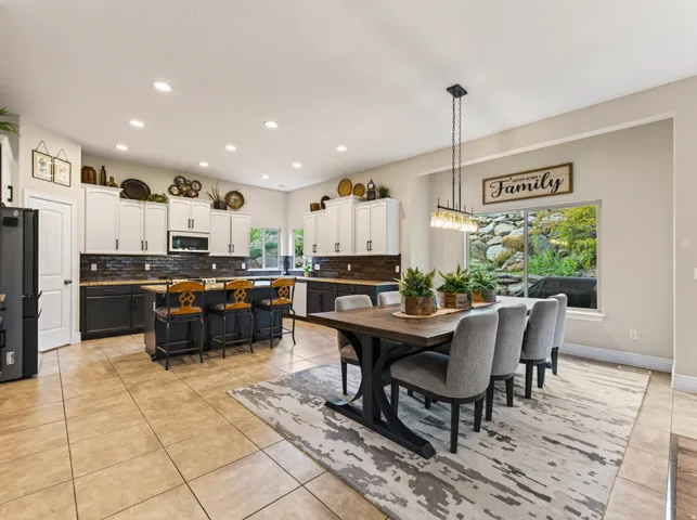 Open-concept kitchen and dining area featuring a two-tone cabinetry design, a central island with bar seating, and a linear pendant light fixture