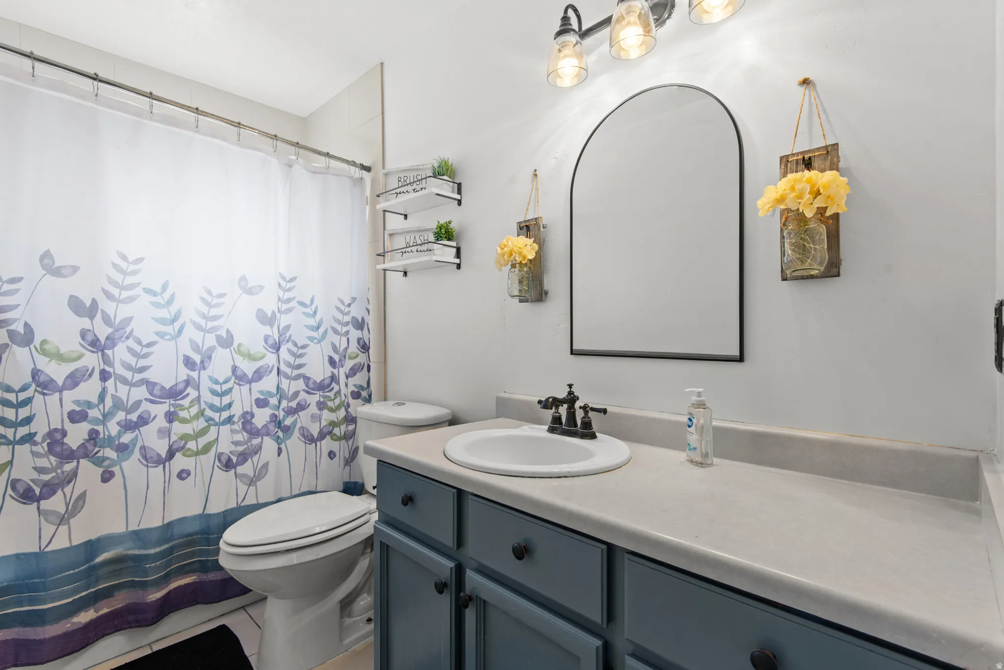 Bathroom featuring a single vanity with a white basin and dark hardware, light-toned countertop, and blue cabinetry