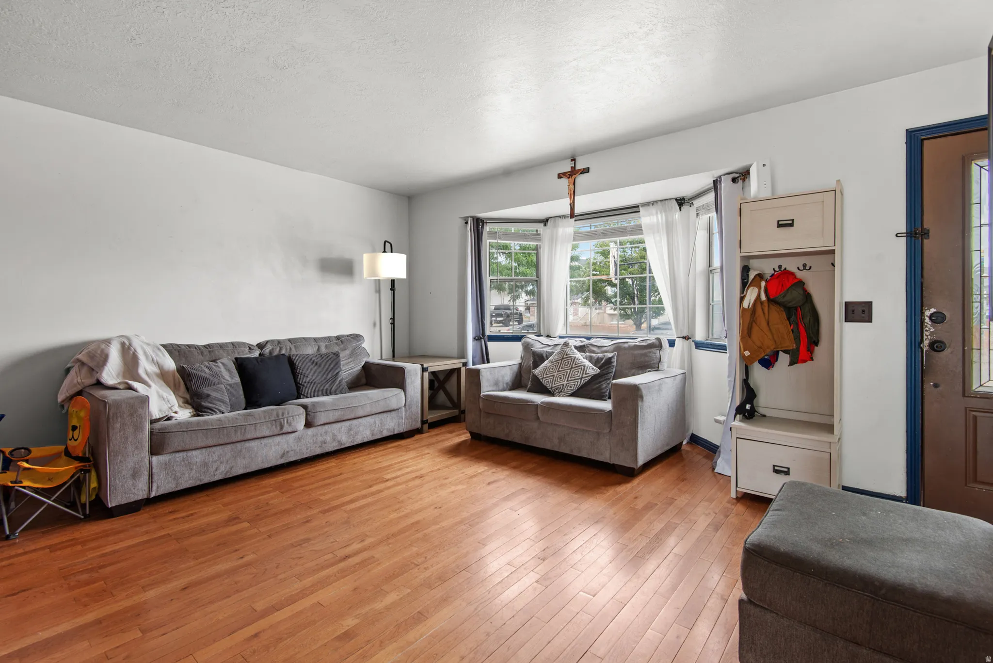 Wood-finish flooring throughout, bay window with multiple panes, white painted walls, and a front entry door with glass insert