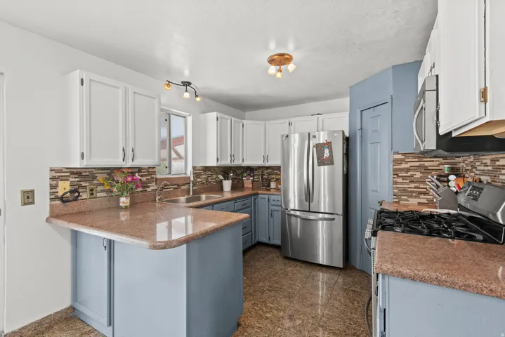 White upper cabinetry with contrasting lower cabinetry, stainless steel appliances, mosaic tile backsplash, and durable tile flooring