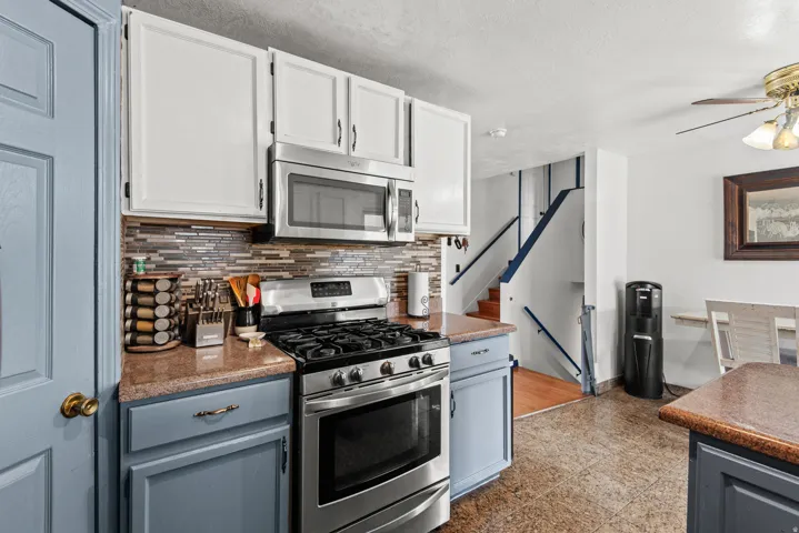 Kitchen featuring stainless steel appliances, mosaic tile backsplash, two-tone cabinetry, and wood-finish countertops