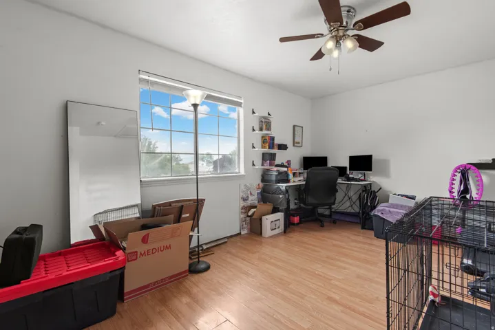 Wood-finish flooring, bright window, ceiling fan with integrated lighting, and wall-mounted shelving