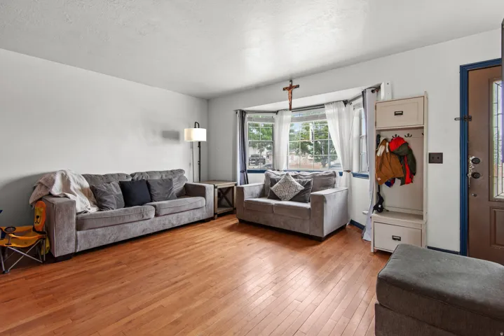 Wood-finish flooring throughout, bay window with multiple panes, white painted walls, and a front entry door with glass insert