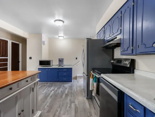 Kitchen featuring blue cabinetry, light-toned countertops, wood-finish flooring, and recessed lighting