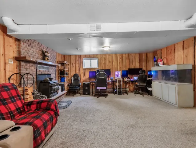 Brick fireplace with a wood-burning stove, wood paneling, and carpet flooring