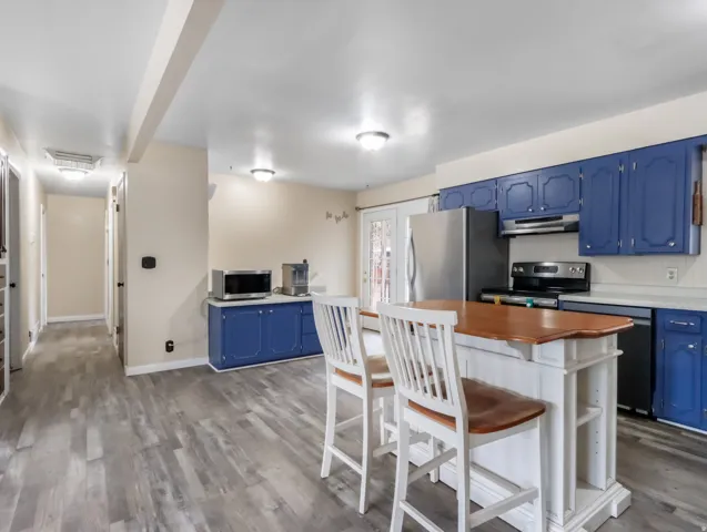 Expansive kitchen featuring wood-finish flooring, blue cabinetry, stainless steel appliances, a center island with seating, and a glass-paned exterior door