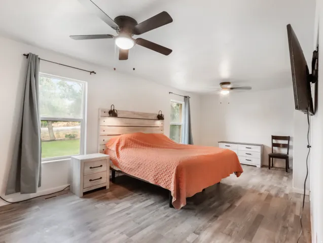 Spacious room featuring wood-finish flooring, multiple windows, and two ceiling fans with integrated lighting