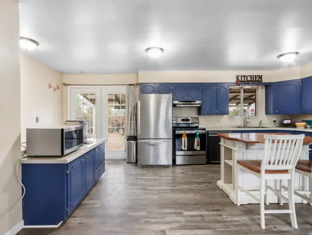 Wood-finish flooring, blue cabinetry, stainless steel appliances, a kitchen island with seating, and French doors