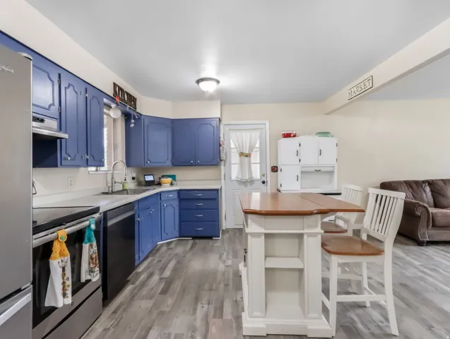 Blue cabinetry with brushed nickel hardware, stainless steel appliances, light-toned countertops, wood-finish flooring, and a white kitchen island with a wood top