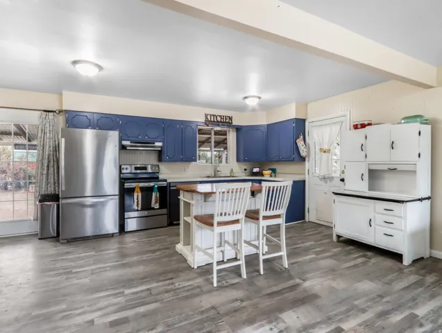 Spacious kitchen featuring wood-finish flooring, stainless steel appliances, blue upper and lower cabinetry, white countertops, and a central island with seating