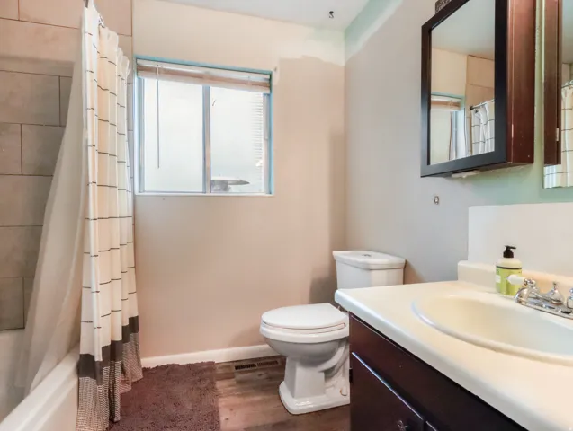 Tub and shower combination with tile surround, wood-finish flooring, and a single vanity with storage
