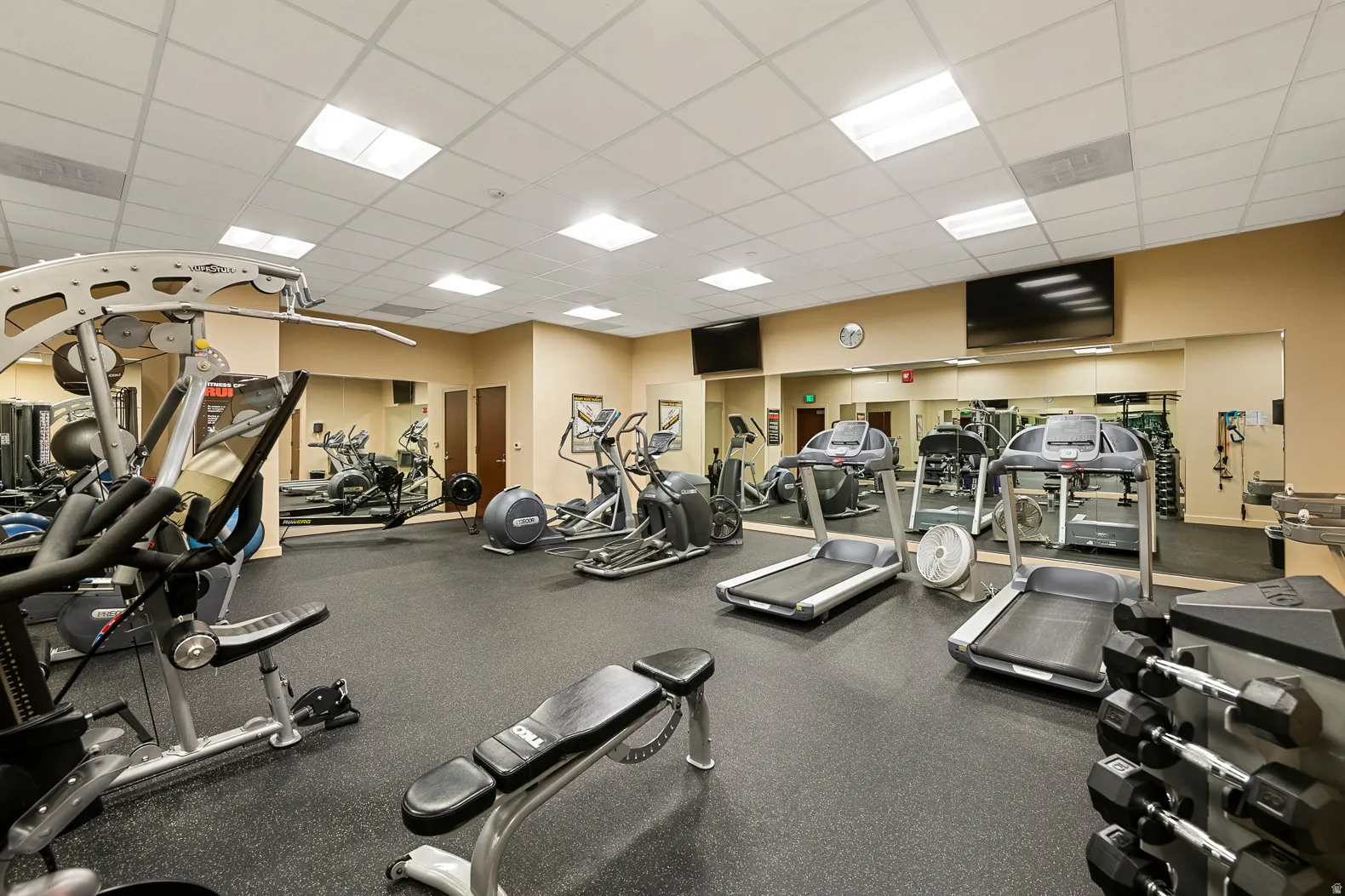 Fitness area featuring rubber flooring, mirrored walls, recessed lighting, and mounted televisions