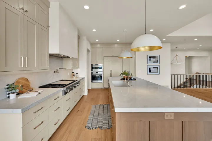 Gourmet kitchen with extensive light-toned cabinetry, a spacious center island featuring an undermount sink, built-in range, and wood-finish flooring