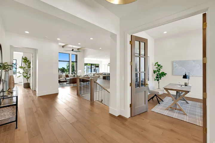 Wood-finish flooring throughout, featuring a bright open-concept living area with large windows, and a dedicated office space with a glass-paneled door