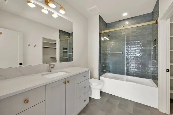 Contemporary bathroom featuring a light gray vanity with a single basin, gold-toned hardware, and a white countertop
