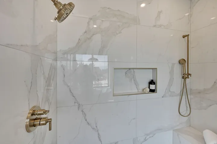 Shower featuring large format wall tile, a built-in niche, and brushed nickel fixtures including a rain showerhead and handheld sprayer