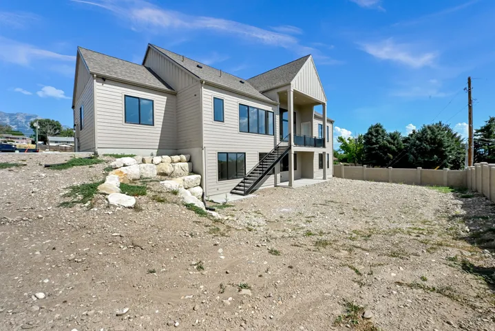 Two-story residence with light-colored siding, a covered upper-level balcony, and a ground-level concrete patio