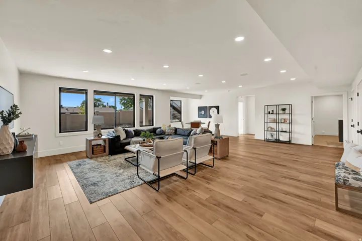 Expansive living area with wood-finish flooring, recessed lighting, and large windows with black framing