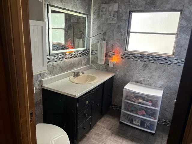 Vanity with an integrated sink, wall-mounted mirror, and tiled walls with decorative mosaic accents