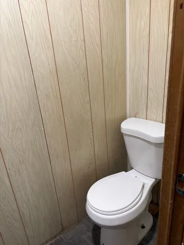 White porcelain toilet with wood-finish paneling and wood-finish flooring