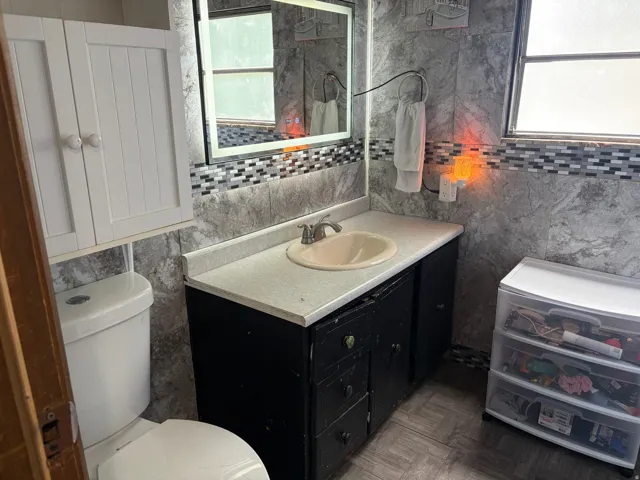 Wall-mounted white storage cabinet, vanity with built-in sink, gray stone-look wall covering, decorative tile accent, and tiled flooring