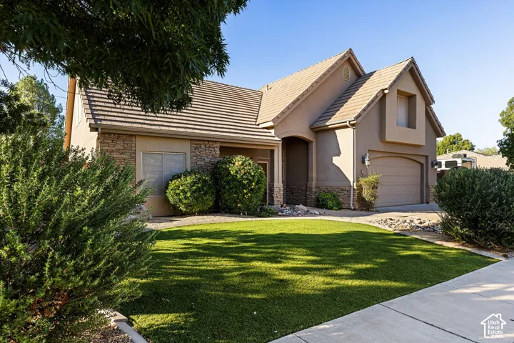 Stucco and stone exterior with a tile roof, an integrated garage, and a lush artificial turf lawn
