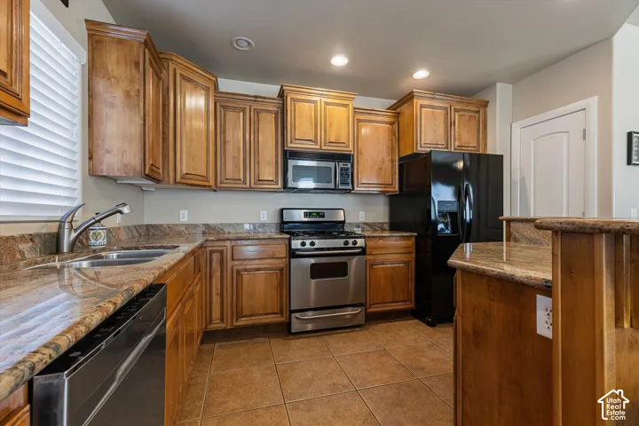 Kitchen featuring wood cabinetry, stone countertops, stainless steel appliances, and recessed lighting